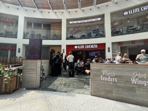 From street facing place. Wooden restaurant barrier on right. Path in centre to entrance. Self ordering screens on left.