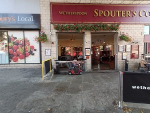 From street, facing venue. Opening ahead to outdoor seating. Archway at back. Restaurant barriers on right.