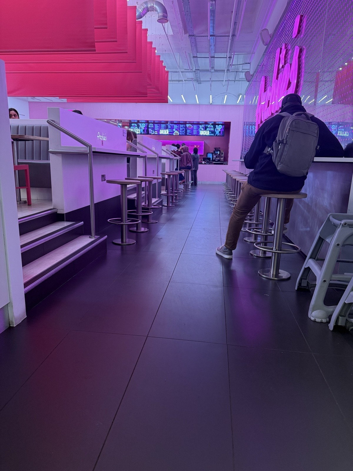 From entrance facing straight. Stairs up to seating on left side. Stools and high tables on right and left side of pathway.