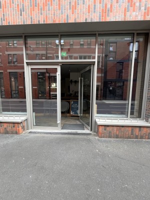 Glass doors with a grey frame and long metal handles in the middle. Push to open.