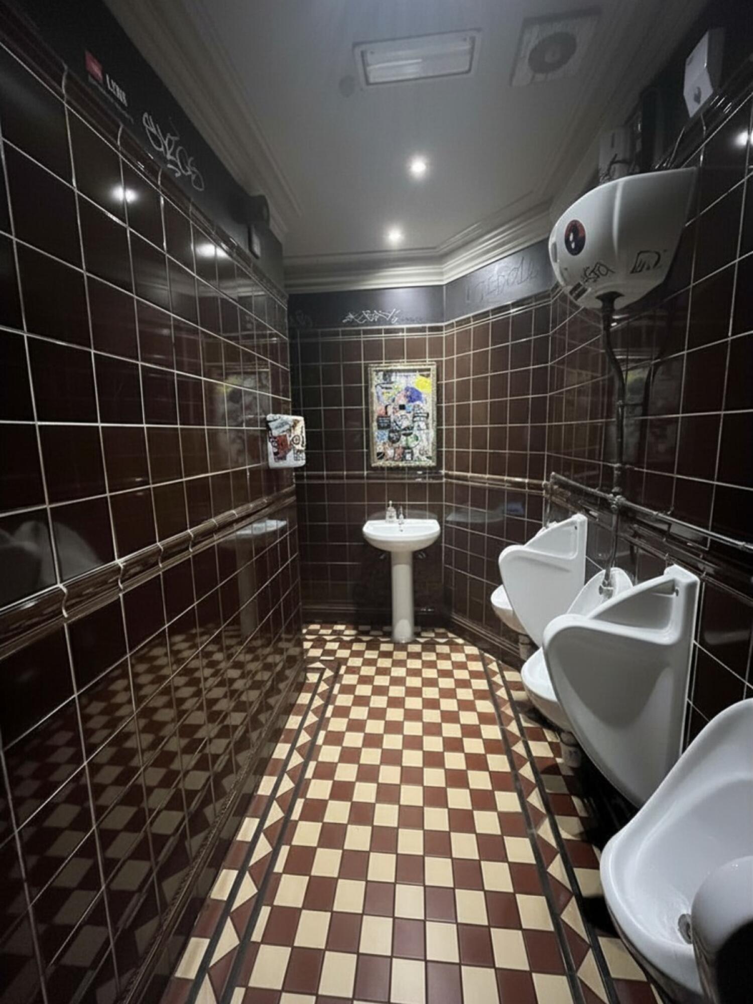 From door facing straight. Urinals on right, sink on back right wall and entrance to toilet on back left.