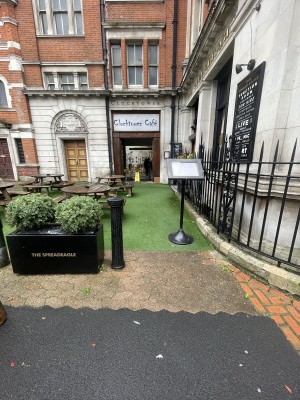 From street facing venue. Menu stand on right. Opening ahead. Planters on left.
