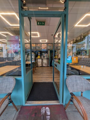 Blue frame door. Push to open. Handle on left. Ramp and small bump at door. Doormat after