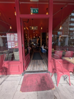 Red frame wooden door. Push to open hand on right. Step and ramp at entrance. Doormat after.