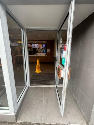 Opening ahead to glass door with metal frame on back. Pull door to open via handle on left.