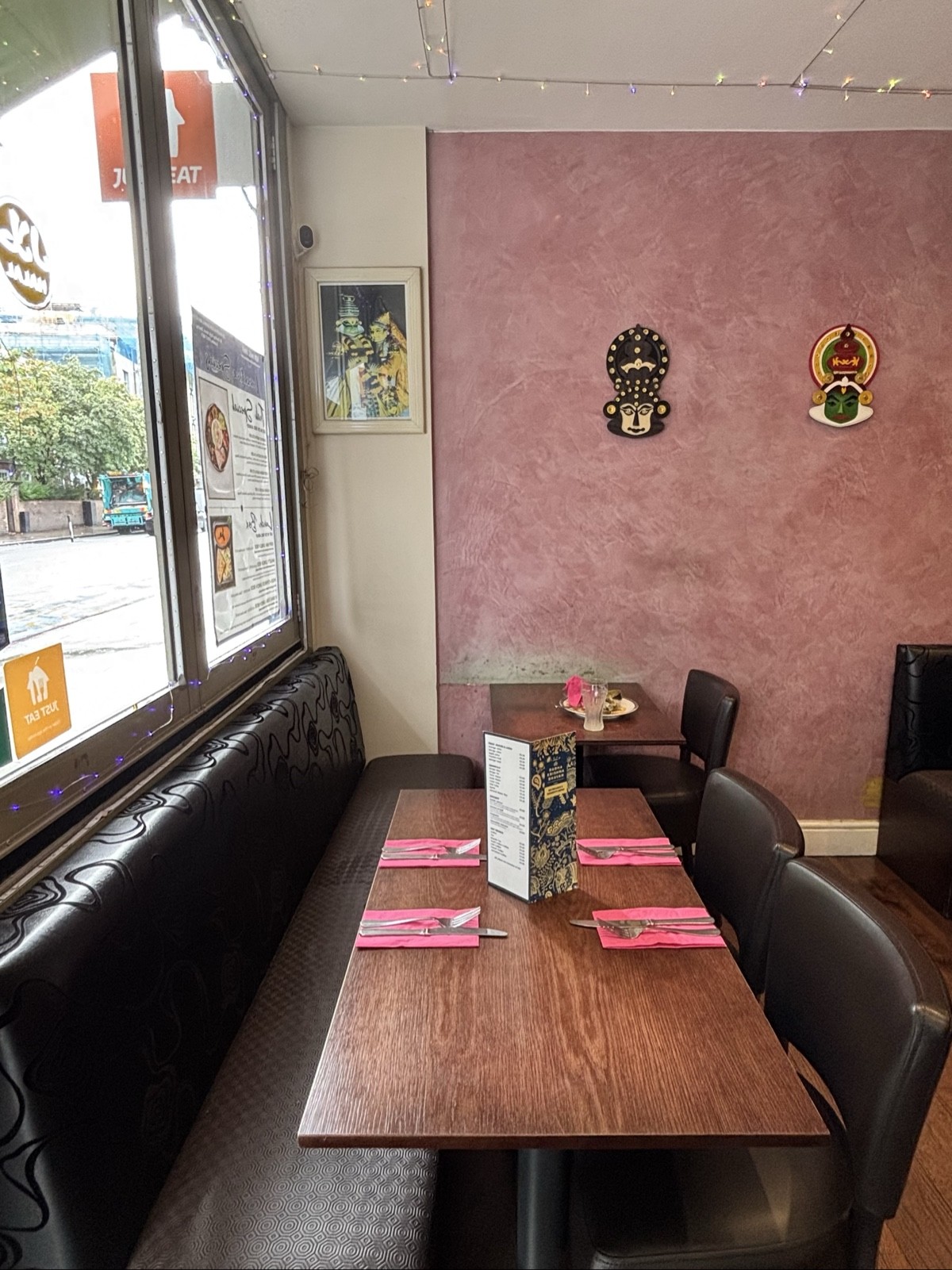 From entrance facing left, glass window to the right. Black half booth below, tables and chairs. Pink wall at the back