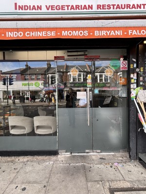 From sidewalk facing straight. Glass walls and glass door. Metal handle to the right, push to open.