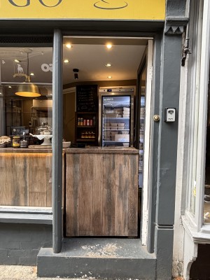 From street facing entrance. Grey doorframe, counter in the middle. Large step at foot of counter