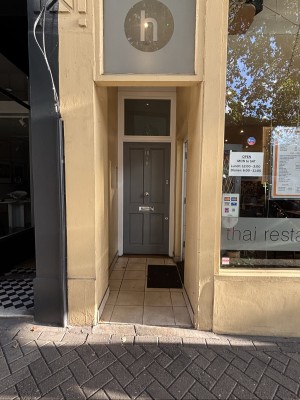 From sidewalk facing straight. Yellow walls, grey door ahead.