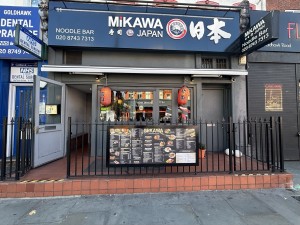 From sidewalk facing venue. Black exterior with red decorative lamps. Black fence lining patio.