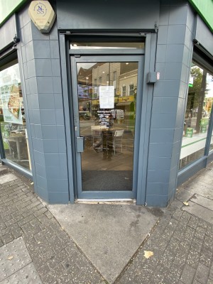 Small step up to the entrance. Blue framed glass door. Push the blue metal handle on left to open.