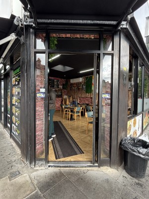 From sidewalk facing straight. Glass and black metal door. Handle on right hand side, push to open.