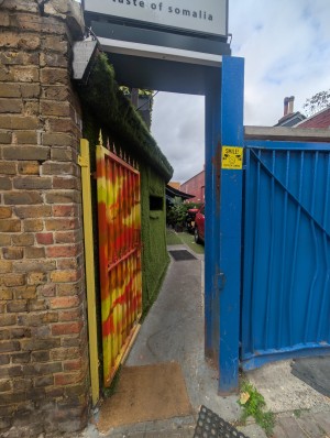 Red, yellow, and blue metal gate. Handle on right. Push to open. Step free. Doormat after.
