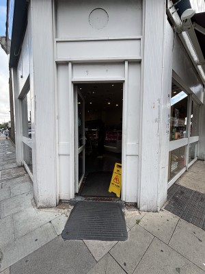 From sidewalk facing venue entrance. White doorframe with glass centre. Yellow caution sign on bottom right