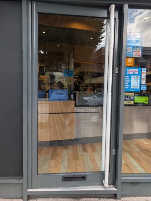 Grey frame door. White metal handle along right. Push to open. Small step at entrance.