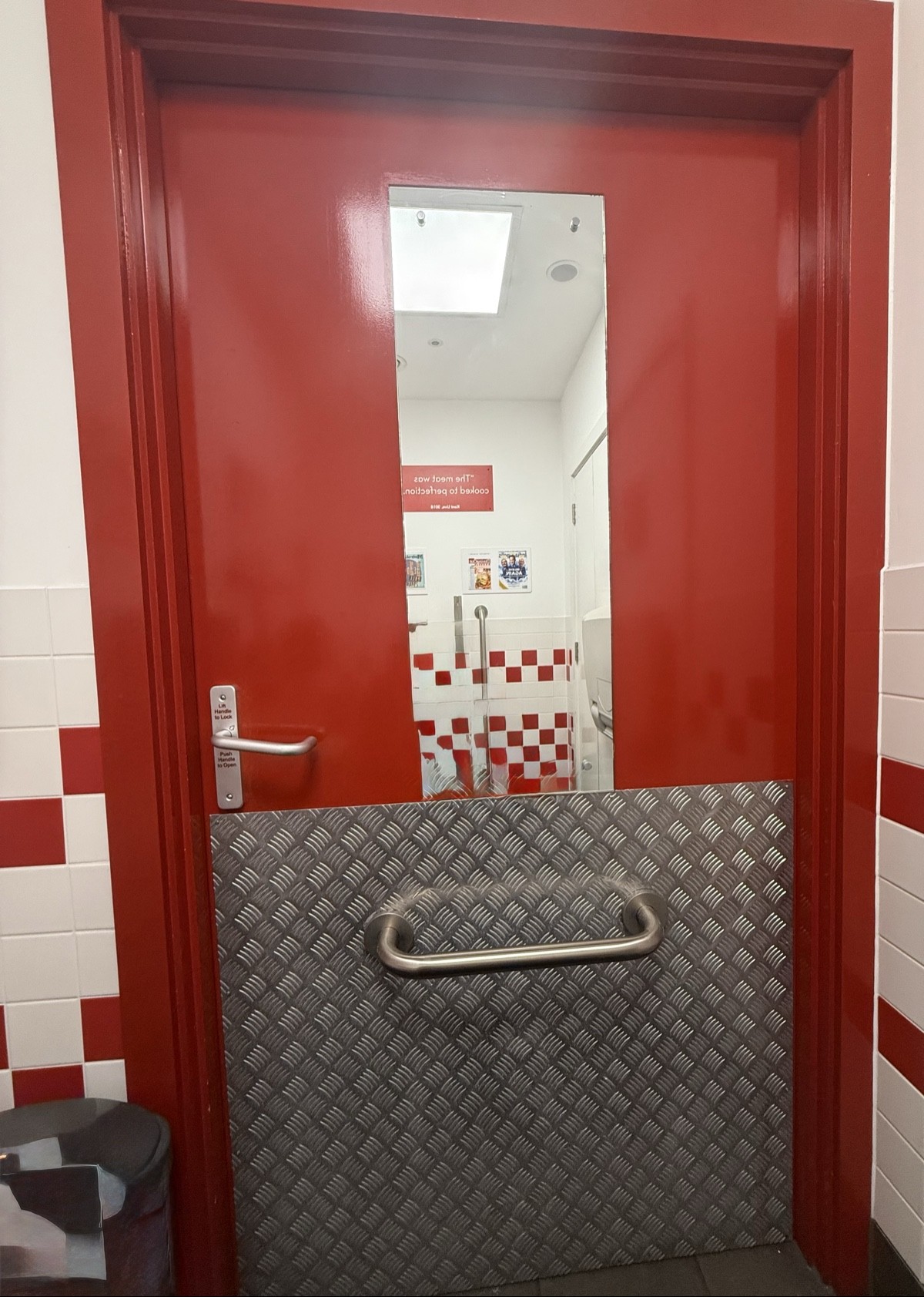Back of toilet door. Lock and handle on left. Metal grab bar central.