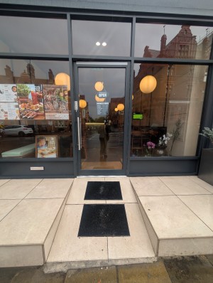 Grey frame door in center. Silver handle on left. Push to open. Ramp to door. Mats present on ramp.