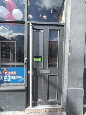 Grey wooden door with glass panel ahead. Push white handle on left to open.
