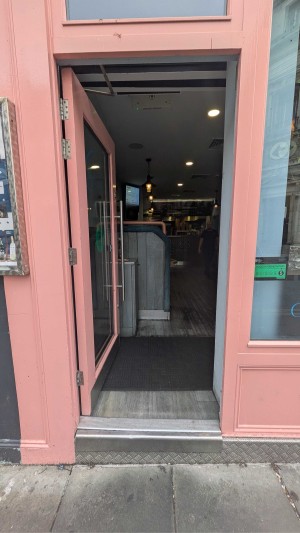 Glass door with a pink frame. Handle on right. Push to open.