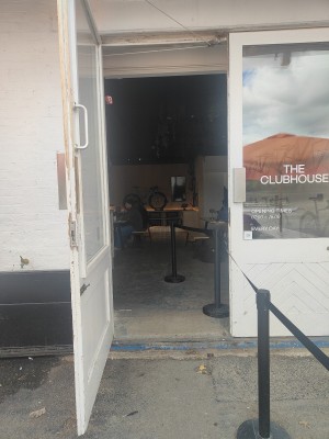 Facing venue entrance. Glass door with wide wooden frame in front. Pull from silver handles in middle to open.