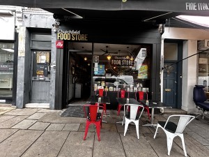 From side walk facing venue. Door on the left. Tables and chairs on the right.