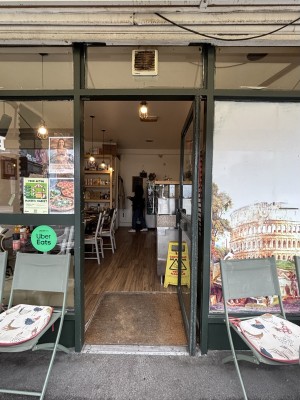 From sidewalk facing venue. Glass door with dark green frame. Door handle to the left, push to open. Glass wall to the left and right.