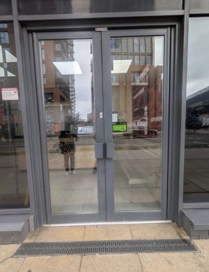Glass doors with grey metal frame ahead. Push from handles in center to open.