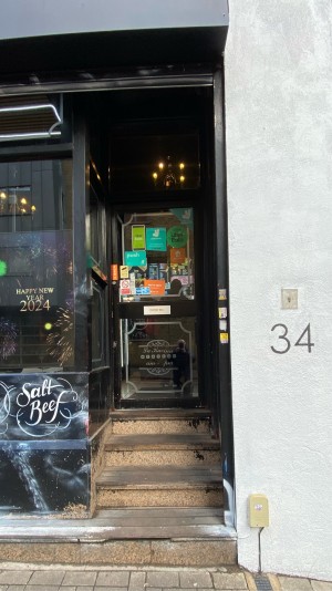 4 steps up to entrance, glass door with black metal frame ahead. Push from left to open.