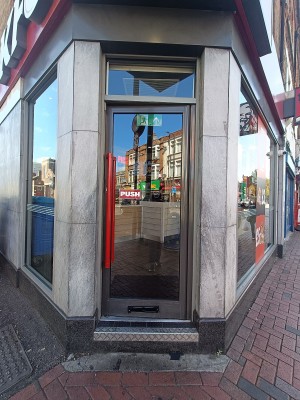 Glass door with black, metal frame. Push from red handle on left to open.