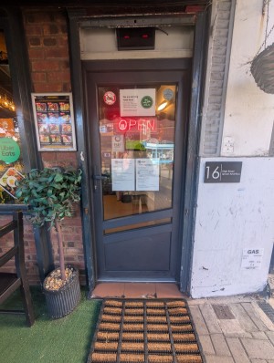 Grey frame door. Handle on left. Push to open. Doormat in front.