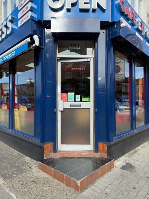 Glass door with grey frame. Push from left to open. Two steps up before door.