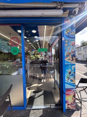 From sidewalk facing venue. Glass door with blue frame ahead. Push metal handle on left to open.
