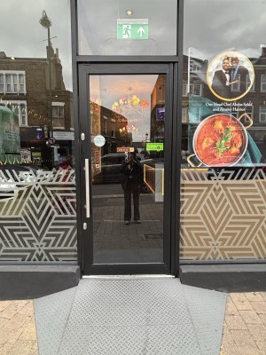 Glass door with black frame, metal door handle on left hand side, push to open.