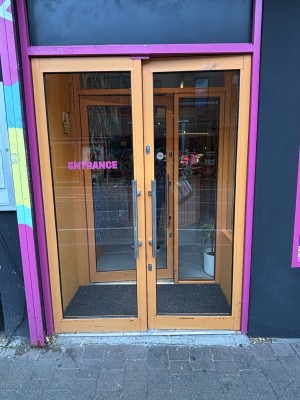 Double glass doors with orange doorframe, metal door handles in the centre, push to open.