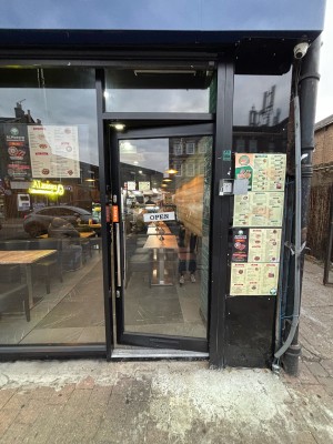 Glass door with black frame. Push door to open via metal handle on left.