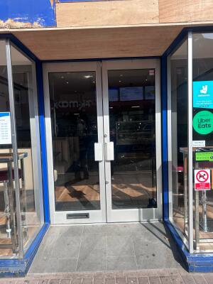 From sidewalk facing venue. Double glass doors with blue frames ahead. Pull handle in center to open.