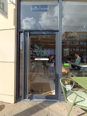 Glass door with black, metal frame. Push from silver handle on left to open.