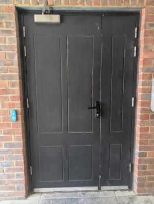 Red brick frame black door. Doorbell for assistance on left. Handle on right center. Pull to open.