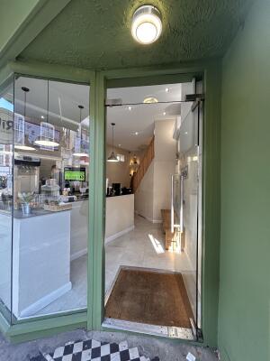 From aidewalk facing venue. Glass door with green metal frames ahead. Push metal handle on left to open.