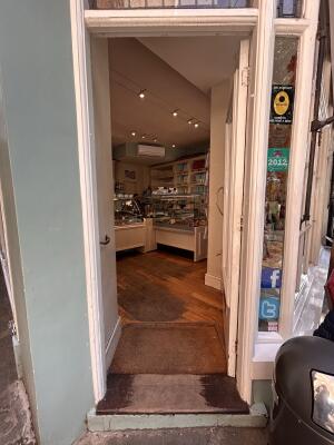 From sidewalk facing venue. Glass door with white frames ahead. Push golden handle on left to open.