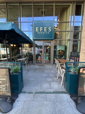 From sidewalk facing venue. Opening ahead between planters. Path behind between outdoors seating to entrance on back.