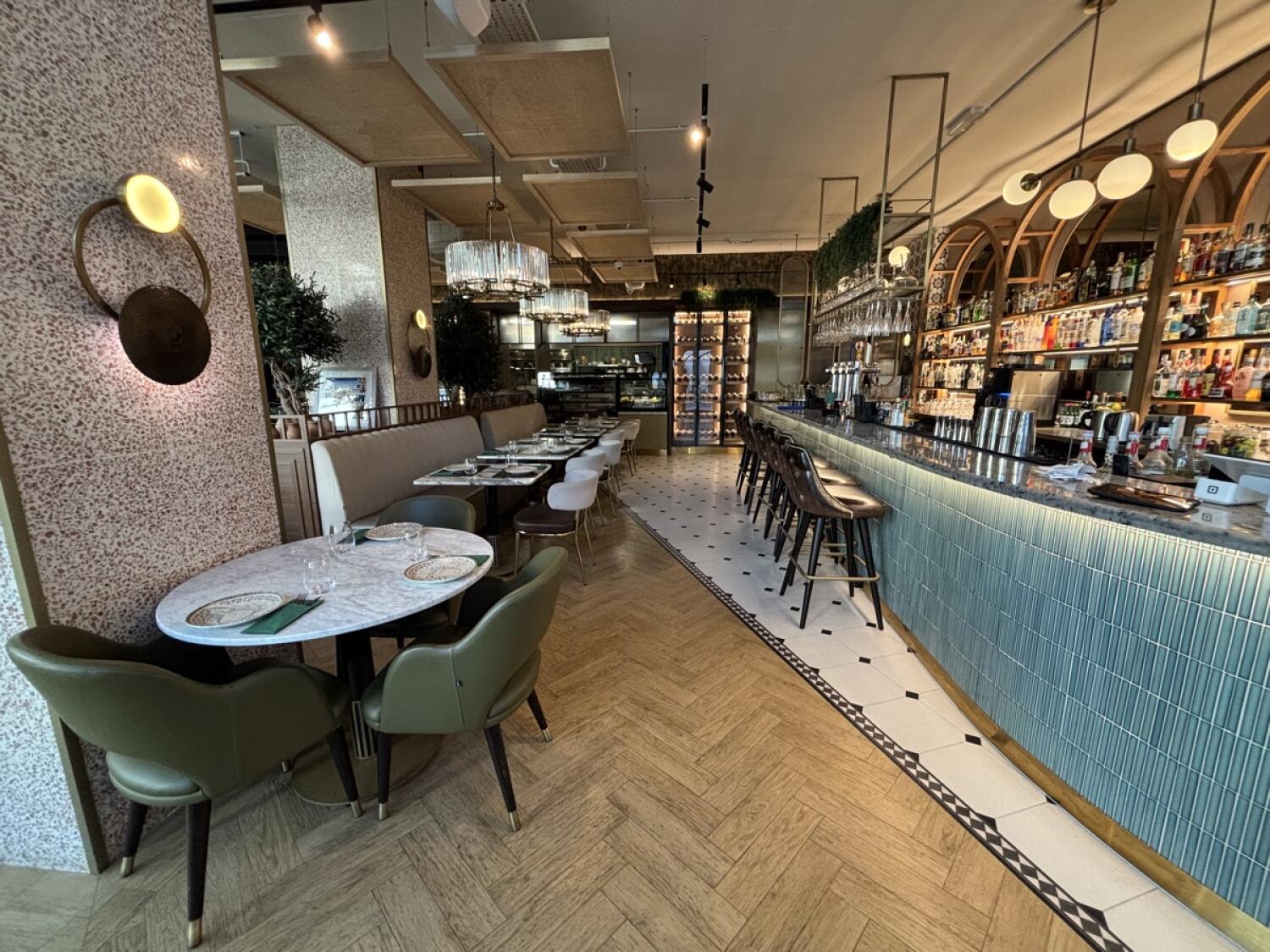 From bar facing straight. Bar with stools along right. Path down center to bathroom on back. Table on left. Half booth with tables and chairs behind.