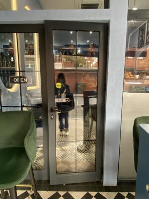 Black framed glass door with black metal handle on left side of door. Turn and pull to open.