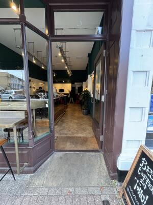 Opening ahead to glass door with brown frame. Push door from metal handle on left to open.