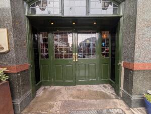 Green wooden doors in front. Gold metal handles in center. Pull to open. Uneven pavement with raised edges in front.