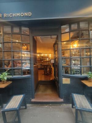 Facing venue. Grey door with glass panels ahead. Push golden bar on left to open.
