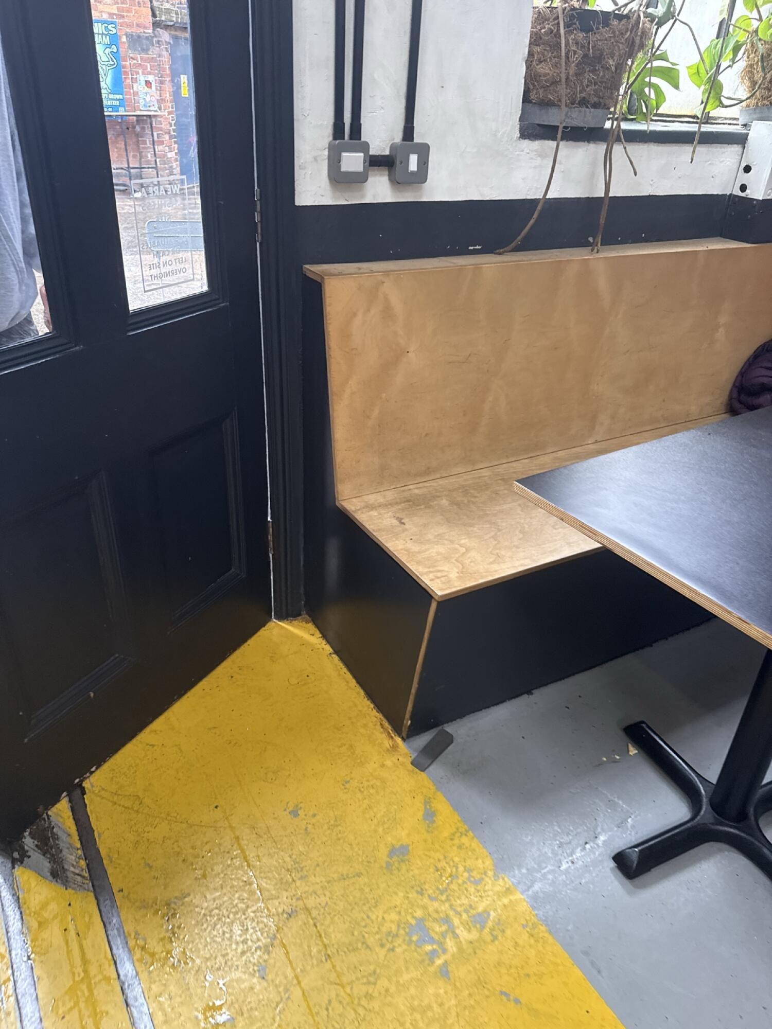 Black wood-framed glass door. Push from handle on left to open. Booth seating with table directly beside door.