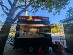 From street facing venue. Black food cart in front. Silver counter along center.