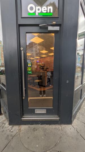 Glass door with grey frame. Push handle on left to open