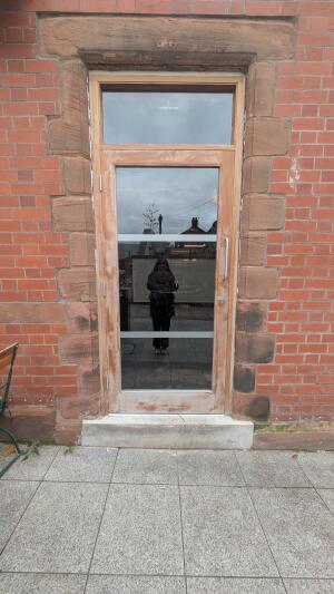 From back left of entrance facing right. Glass door with wooden frame. Pull handle on right to open.